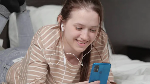 Das Mädchen spielt zu Hause mit einem mobilen Gerät. Eine schöne junge Frau kommuniziert mit ihrem Smartphone im Internet, lacht, surft in sozialen Netzwerken, spielt Handyspiele, sitzt auf der Couch. — Stockfoto