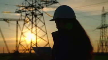 İnşaat mühendisi, kadın elektrik tedarikçisi açık havada çalışıyor. Çevre dostu elektrik. Modern teknolojiler. Güvenlik kaskındaki güç mühendisi güç hattını ve dijital tableti kontrol ediyor.