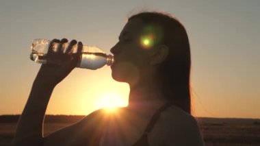 Kadın doğadaki eğitimden sonra şişeden serinletici su içiyor. Açık hava sporları, kız gün batımında güneş altında idmandan sonra temiz maden suyu içiyor. Susuzluğunu soğuk suyla bastır.