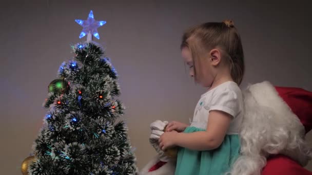 Barn, flicka och jultomten dekorera julgranen med vackra leksaker. Liten bebis och jultomten hänger vackra bollar på julgranen. Familjens barn vintersemester. God jul.. — Stockvideo