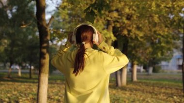 Genç bir kadın, aktif bir atlet kulaklık takıyor, müzik dinliyor, koşuyor, parkta antrenman yapıyor. Koş ve kilo ver. Şehir parkındaki ağaçların arasında koşan sporcu kız. Kadın, koşu, spor, güç.