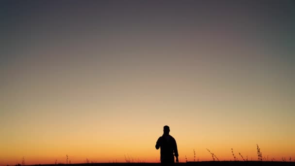 Een arbeider met een schop loopt bij zonsondergang door de plantage. Landbouwbedrijf, landbouw. Silhouet van een boer met schop in zijn handen gaat door het veld van het werk. Groenten verbouwen — Stockvideo