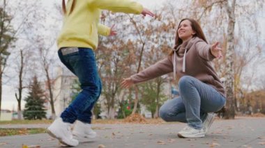 Mutlu bebek sonbahar parkında koşup annesine sarılıyor. Anne ve kızı sonbaharda çocuk parkında birlikte oynuyorlar. Anne, sevgili kızına sarılıyor. Anneler Günü konsepti