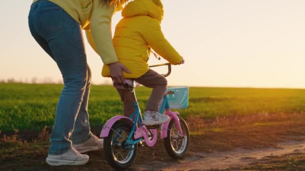 Familia feliz, niño y mamá, el niño aprende a andar en bicicleta en el parque al atardecer. Madre enseña a su hija, hijo a montar en bicicleta infantil en la carretera de otoño. Familia joven y feliz, infancia, estilo de vida activo — Vídeo de stock