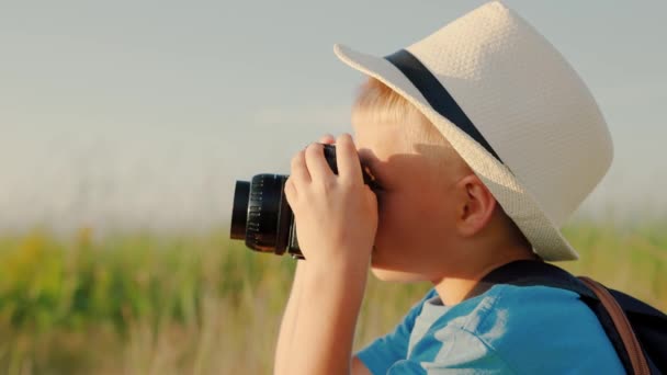 Um garotinho bonito está segurando a câmera vintage e tirando fotos da natureza. Rapaz feliz sonha em tornar-se fotógrafo. O miúdo joga no parque no Verão, na Primavera. Criança sonha em viajar, fazer descobertas — Vídeo de Stock