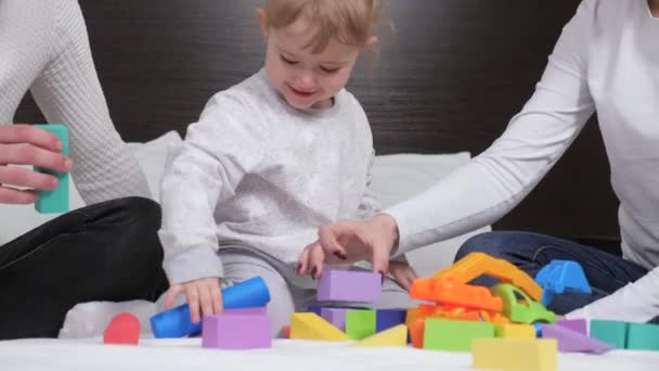 Glückliche Familie, Lernspiele für Kinder. Unterrichten eines Kindes durch Spielaktivitäten. Papa, Mama, Tochter spielen mit Würfeln im Kinderzimmer auf dem Bett. Kind, Vater und Mutter spielen beim Hausbau. — Stockvideo