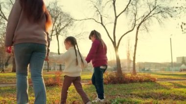 Anne ve çocuklar, kızlar parkta el ele tutuşarak yürüyor. Mutlu aile sonbaharda parkta yürüyüş yapar. Mutlu sağlıklı aile kavramı. Anne ve çocuklar birlikte dışarı çıkıyorlar. Aile hafta sonu parkta