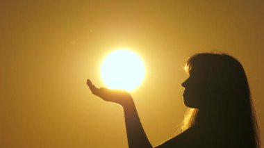 Mutlu kadın avuçlarında güneş tutuyor. Güneş ışığı kızların elinde. Gün batımında dua eden bir kızın silueti. Seyahat ve macera konsepti. Güneşin ihtişamını takdir et. Din ve Tanrı 'ya inanç.