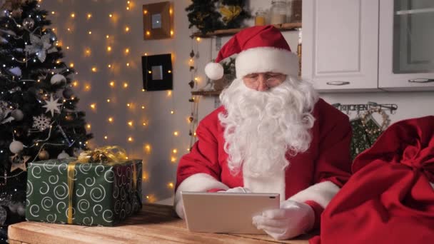 Санта Клаус работает с цифровыми планшетами. Санта, технологии. Современное устройство в руках Санты. Рождество. Новогодний семейный праздник. СантаКлаус пользуется планшетным компьютером, проверяет список подарков для детей. — стоковое видео