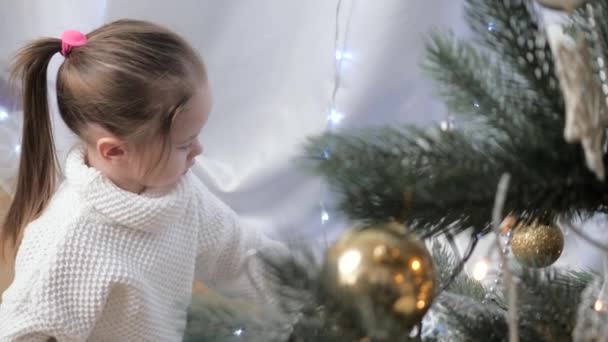 Un enfant pend une boule de jouet dorée sur un arbre de Noël. Belle petite fille décore l'arbre de Noël avec des boules colorées. Bonne famille, enfance, Noël. Il joue le soir de Noël. Célébration — Video
