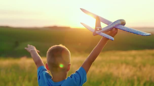 Um menino brinca com um avião de brinquedo, corre no parque através de um campo ao pôr-do-sol e quer se tornar um astronauta. Conceito de sonho de liberdade. O garoto brinca com seu brinquedo favorito de avião no verão — Vídeo de Stock