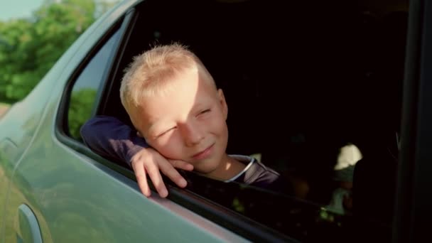 Szczęśliwy chłopiec podróżuje samochodem patrząc przez okno samochodu. Letnia podróż rodzinna prywatnym transportem. Młody chłopiec marzy i uśmiecha się. Dzieciak podróżuje z rodziną. Szczęśliwa rodzina podróżuje samochodem. — Wideo stockowe