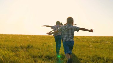 Çocuklar gün batımında yaz parkında birlikte koşu oynuyorlar. Mutlu aile. Parkta insanlar, doğada oğulları olan aile tatili, neşeli koşu. Küçük çocuklar uçmayı, uçmayı, fantezileri hayal eder.