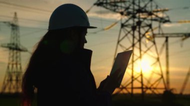 İnşaat mühendisi, elektrik tedarikçisi açık havada dijital tabletle çalışıyor. Çevre dostu elektrik. Modern teknolojiler. Kasklı bir güç mühendisi güç hattını kontrol ediyor.