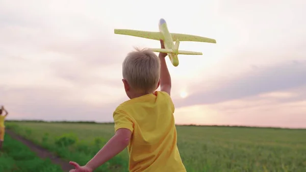 Fröhliche Kinder toben im Park und spielen im Sommer in der Natur mit Spielzeugflugzeugen. Junge läuft mit Spielzeugflugzeug auf Weizenfeld Glückliche Familie. Jungen träumen vom Fliegen. Sorgenfreies Kind beim Spielen im Freien — Stockfoto