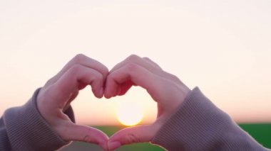 Gün batımında kalp sembolü olan, hayatta özgürce seyahat eden, gün ışığını seven romantik bir adam, gökyüzünün arka planında sevgililer günü kartı figürü yapan, sağlık jesti