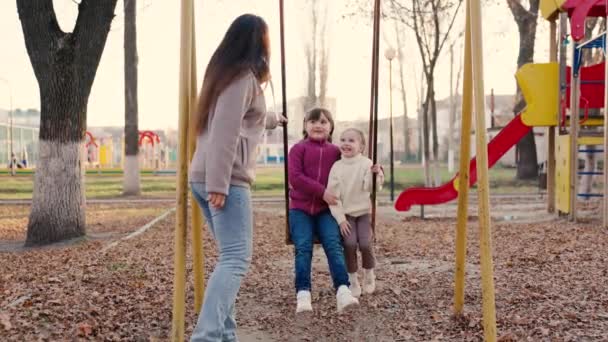 Mother shakes little daughters child swing in an autumn park, happy family, childrens laughter on walk city park, kid is having fun, smiling, flying up, oktivny rest healthy baby, entertaining walks — Stock Video