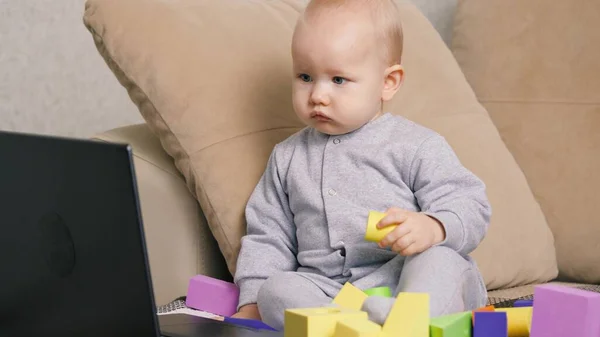 El niño juega con juguetes en casa en el sofá junto a su madre. Familia feliz en casa. El chico juega y mira la computadora. Educación moderna. Pequeño hijo, hija jugando con juguetes —  Fotos de Stock