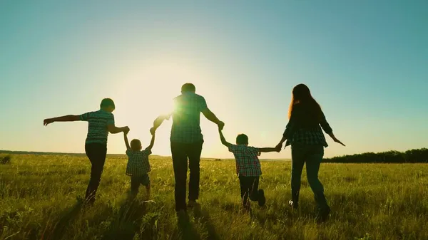 Mutlu aile, aileler, çocuklar parkta koşuyor. Büyük mutlu aile kavramı. Aile yürüyüşü, gün batımında ebeveynlerin ve çocukların silueti. Anne baba, oğullar birlikte yürür. Aile tatili, hayaller