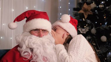 Noel Baba kucağında oturan bir kızla oynuyor. Kızım, çocuk Santaclaus için bir dilek tutuyor. Noel arifesi, aile çocukları tatil konsepti. Evde Noel partisi var. İyi tatiller.