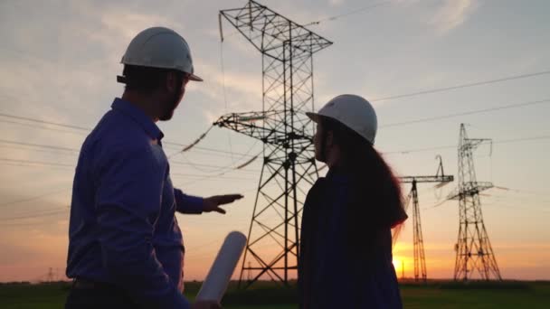 Dva stavební inženýři spolupracují na elektrickém přenosovém vedení. Týmová práce energetických inženýrů v ochranných přilbách, údržba vedení pod širým nebem. Kolegové si podávají ruce. — Stock video
