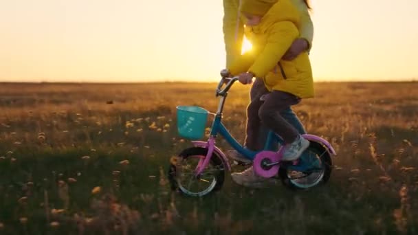 Matka uczy dziecko, córkę, syna na polu jesienią jeździć na rowerze dla dzieci. Szczęśliwa rodzina, dziecko i mama, dziecko uczy się jeździć na rowerze w parku o zachodzie słońca. Aktywna młoda rodzina na świeżym powietrzu — Wideo stockowe