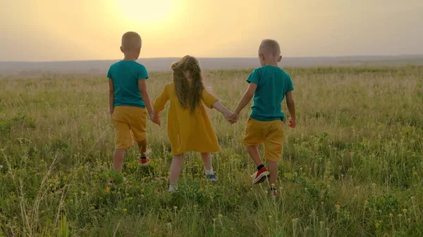 Kinder, Jungen, ein Mädchen laufen händchenhaltend über das Feld. Kindheitsfreunde reisen in die Natur, Kindheitsträume. Eine Gruppe von Kindern spielt gemeinsam im Park. Kindheitsfreundschaftskonzept — Stockfoto