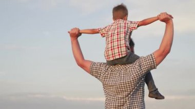 Oğlu babasının boynuna oturur, pilotu oynar, süper kahraman olarak uçar. Baba ebeveynliği konsepti. Mutlu baba ve küçük çocuk oynuyorlar, bir çocukla rüya görüyorlar. Mutlu aile parkta dinleniyor..