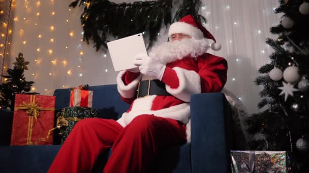 Santa Claus pracuje s digitálním tabletem a připravuje dárky pro děti. Moderní věcička v rukou Santy. Vánoce. Novoroční rodinná dovolená. Santa Claus používá tablet počítač — Stock video