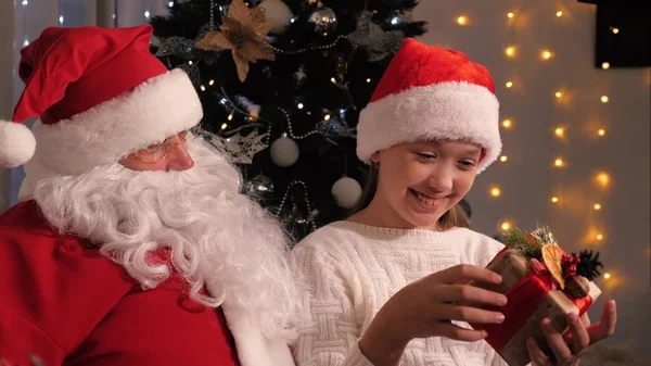 Papai Noel deu um presente para uma menina, feriado de Natal. A criança está segurando um presente do Papai Noel e está feliz. O conceito de férias de crianças de inverno e celebrações. Feliz noite de Natal — Fotografia de Stock