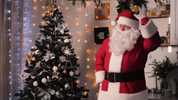 Wigilia, Święty Mikołaj tańczy w urządzonym mieszkaniu w pobliżu choinki z kulkami i światłami. Koncepcja rodziny, wakacje dla dzieci. Wesoły Mikołaj świętuje nowy rok w domu. — Wideo stockowe