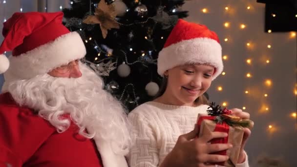 Jultomten gav en julklapp till en flicka. Barnet håller en gåva från tomten och är lycklig. Begreppet vinter barn semester och firande. Grattis på julafton — Stockvideo