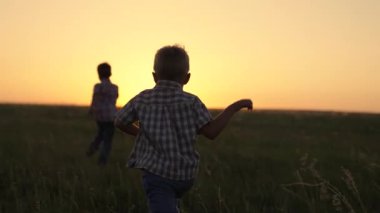 Arkadaşlar sahadaki yeşil çimlerde koşar. Çocukların mutluluğu, hayalleri. Siluet, mutlu çocuklar, gün batımında parkta birlikte koşan çocuklar. Çocuklar yazın dışarıda oynarlar.