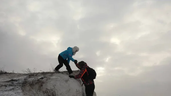 Poutníci lezou na skálu společně. Týmová práce obchodníků. Obchodní tým vyhrává. Turističtí horolezci muž a žena natahují ruce k sobě, pomáhají vylézt na vrchol kopce. — Stock fotografie