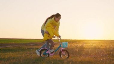 Mutlu aile, çocuk ve anne, çocuk gün batımında parkta bisiklet sürmeyi öğreniyor. Anne, kızına ve oğluna sonbaharda çocuk bisikleti sürmeyi öğretiyor. Mutlu aktif genç aile, çocukluk
