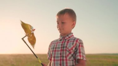Küçük bir çocuk elinde oyuncak bir rüzgar türbiniyle gün batımında bir oyun parkında oynuyor. Çocukluk kavramı, Aile. Mutlu bir çocuk, baharda parkta pikap oyuncağıyla oynar.
