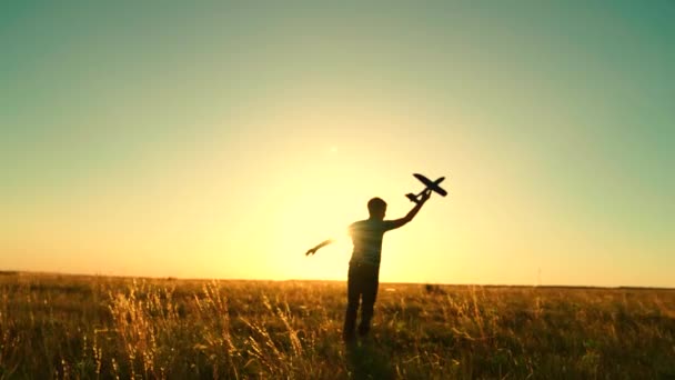 Silhouet van een gelukkig kind loopt met een speelgoedvliegtuig bij zonsondergang op het veld. Droomconcept. De jongen droomt ervan piloot te worden, astronaut. Kinderfantasie, kind rent met een speelgoedvliegtuig. — Stockvideo