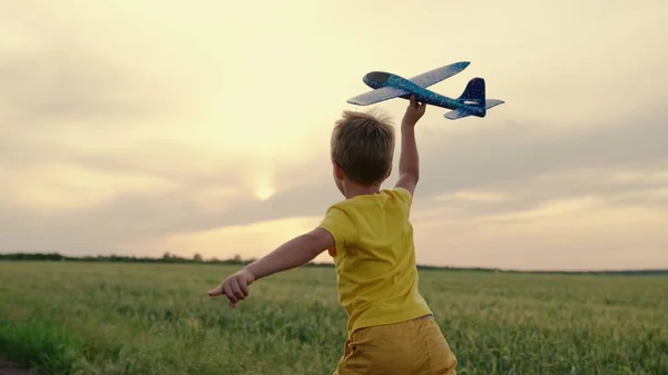 Мальчик бегает на игрушечном самолете по пшеничному полю. Счастливый ребенок бегает по парку, летом на природе играет с игрушечным самолетом. Счастливая семья. Мальчик мечтает летать. Беззаботный ребенок играет на открытом воздухе — стоковое фото