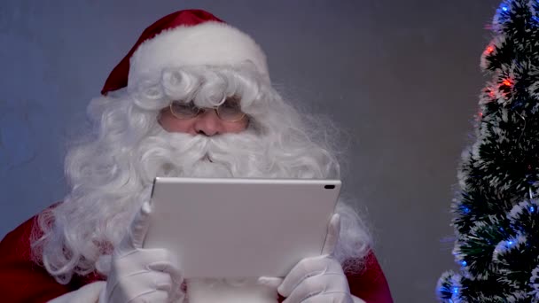 Babbo Natale lavora da remoto da un tablet online la vigilia di Natale. Buon Babbo Natale sorridente e guardando tablet moderno a casa. Vacanze di Capodanno. Inverno famiglia bambini vacanza concetto — Video Stock