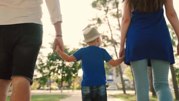 Pap, zoon, mam loopt en houdt elkaars hand vast in de stad in de zon. Gelukkige familie wandelingen met een kind in het park in een rustige straat in de zomer. Gelukkige ouders en kinderen. Familieweekendconcept — Stockvideo