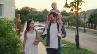 Anne ve kızı babalarının omuzlarında sessiz bir caddede yürüyorlar. Mutlu aile yaz parkında bir çocukla yürüyor. Mutlu ebeveynler ve çocuklar dışarıda. Aile hafta sonu konsepti