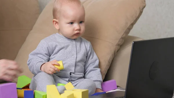 这孩子看着电脑，很淘气，哭着。妈妈用笔记本电脑教她的小孩。现代母性。一个工作的自由母亲和她的孩子在沙发上玩耍。妈妈和小儿子在家里 — 图库照片