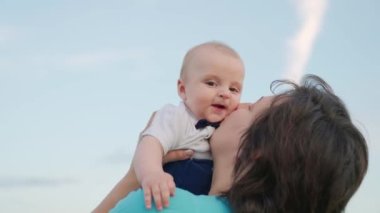 Mutlu aile, küçük bebek ve anne mavi gökyüzüne karşı parkta birlikte oynuyorlar. Anne ve çocuk yazın çocuk parkında yürürler. Bebek ve annesi sarılıp öpüşüyor. En sevdiği çocuk, çocukluk.