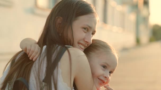 Genç bir anne sevgili küçük kızına nazikçe sarılır, çocuk güler ve gülümser. Mutlu aile yazın sokakta yürüyor. Çocuk bahar parkında annesine sarılıyor. Küçük kız ve anne yakın çekim — Stok video