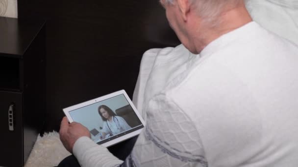 Пожилой человек заболел, используя электронную табличку дома, чтобы поговорить со своим врачом. Профессиональный врач лечит пациента в онлайн видео чате. Приложение для видеоконференций. Семейный врач — стоковое видео