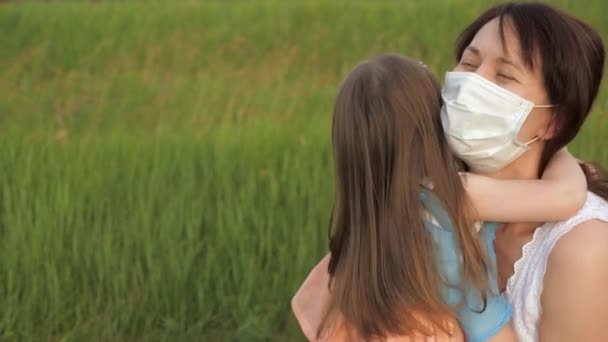 Mère apprend à sa fille à mettre un masque protecteur. Maman joue avec l'enfant dans le parc en été dans la rue pendant l'épidémie de coronavirus. Bonne famille maman, fille câlins, baisers — Video