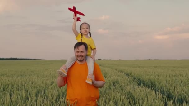 Mutlu aile, kız ve baba buğday tarlasında birlikte oynuyorlar. Çocuk elinde oyuncak bir uçak tutuyor. Çocukluk hayali olan uçma ve pilot olma fikri. Baba ve çocuk. — Stok video