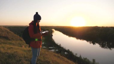 Kaygısız neşeli kız doğada dijital tabletle seyahat ediyor. Dağın tepesinde tablet bilgisayar kullanan genç bir turist blogcusu. Çok güzel bir manzarası var..