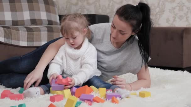 Juegos educativos para niños. Mamá, el niño está jugando con cubos en la guardería en el suelo. Enseñar a un niño a través del juego. Madre e hija están jugando a construir una casa familiar. Una familia feliz. — Vídeo de stock