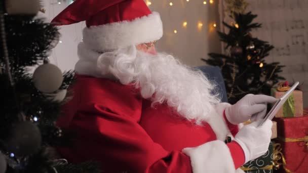 Papai Noel trabalha com tablet digital. gadget moderno nas mãos do Papai Noel. No Natal. Férias de família de Ano Novo. SantaClaus usa tablet computador, verifica sua lista com presentes para crianças. Santa, tecnologia — Vídeo de Stock